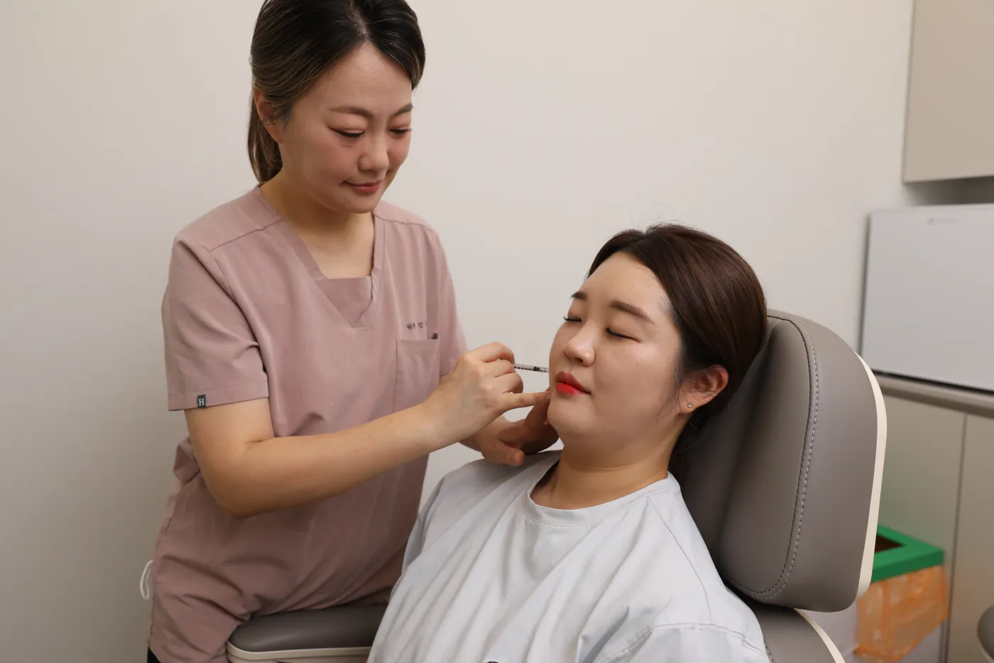 진료 의자에 앉은 환자의 턱선에 주사 시술을 하는 안우경 대표원장